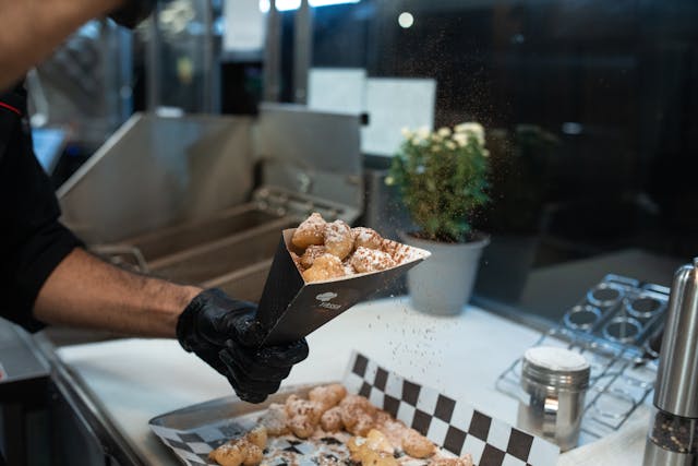 Man powdering a serving of beignets with cocoa.