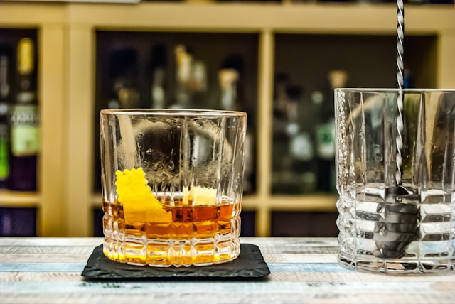 Close-up of a glass of Sazerac on a black coaster.