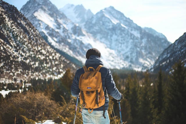 Man in a blue jacket and a yellow backpack hiking in the mountains.