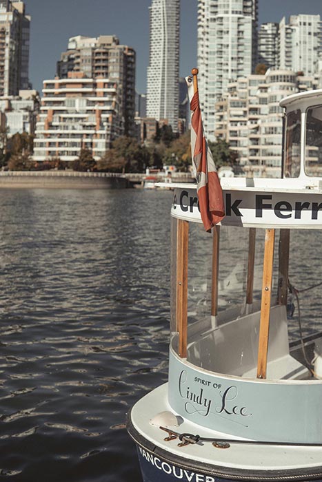 A small ferry boat with a Canadian flag docked in Vancouver’s harbor, with high-rise buildings in the background.